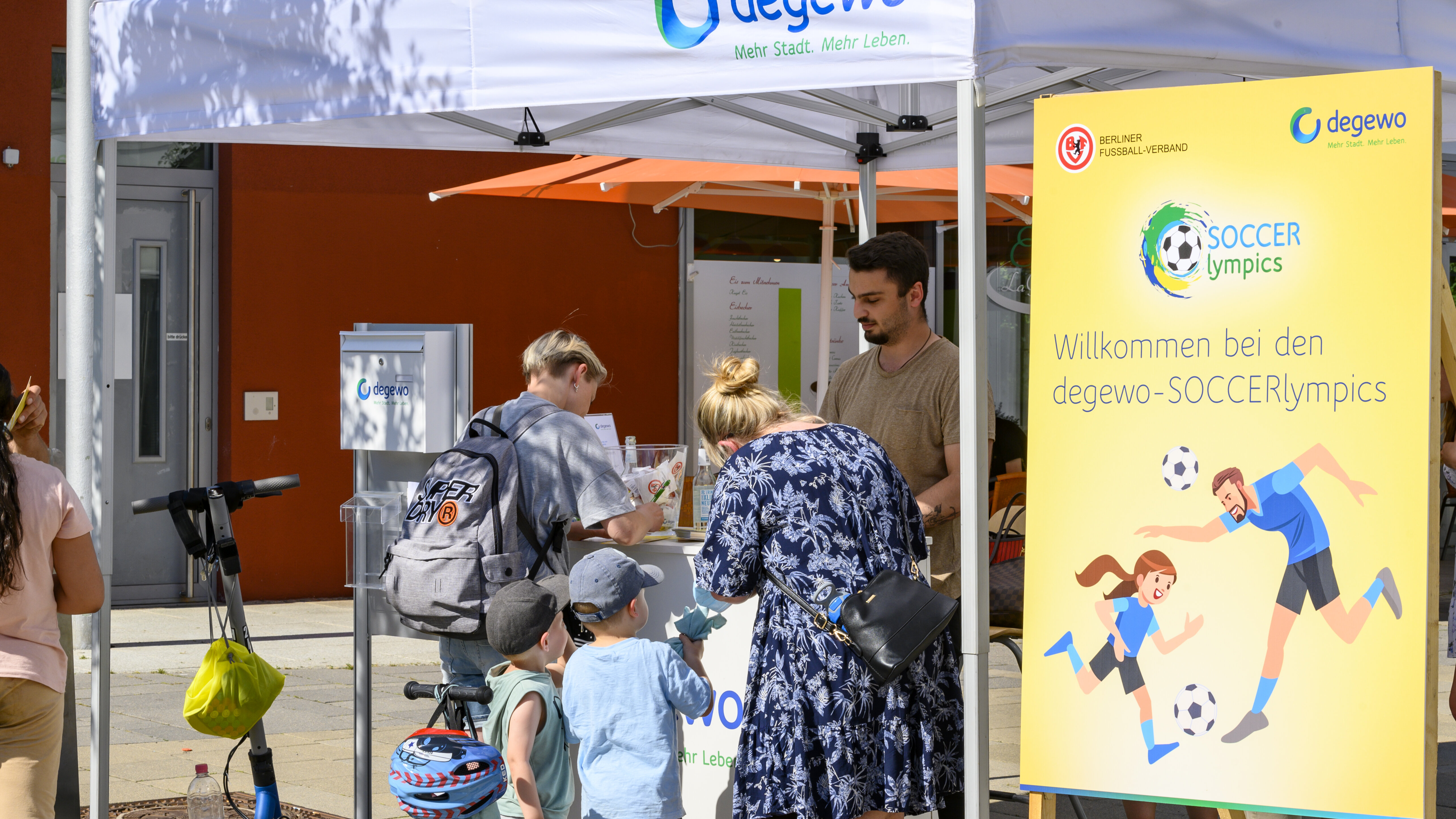 Menschen stehen an einem Infostand unter einem Zelt bei einer Veranstaltung im Freien.