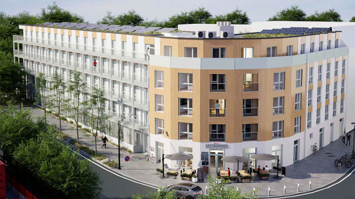 Visualisierung eines modernen, fünfgeschossigen Wohn- und Geschäftshauses an einer Straßenecke. Die Fassade kombiniert helle Putzflächen mit vertikalen Holzelementen, darüber ein zurückgesetztes Staffelgeschoss. Auf dem Dach sind Photovoltaikanlagen und Technikaufbauten zu sehen. Im Erdgeschoss befindet sich eine Gastronomie mit Außenterrasse; in den oberen Etagen verfügen die Wohnungen über Balkone. Straßenbäume, Fahrräder und Passanten beleben das Umfeld.