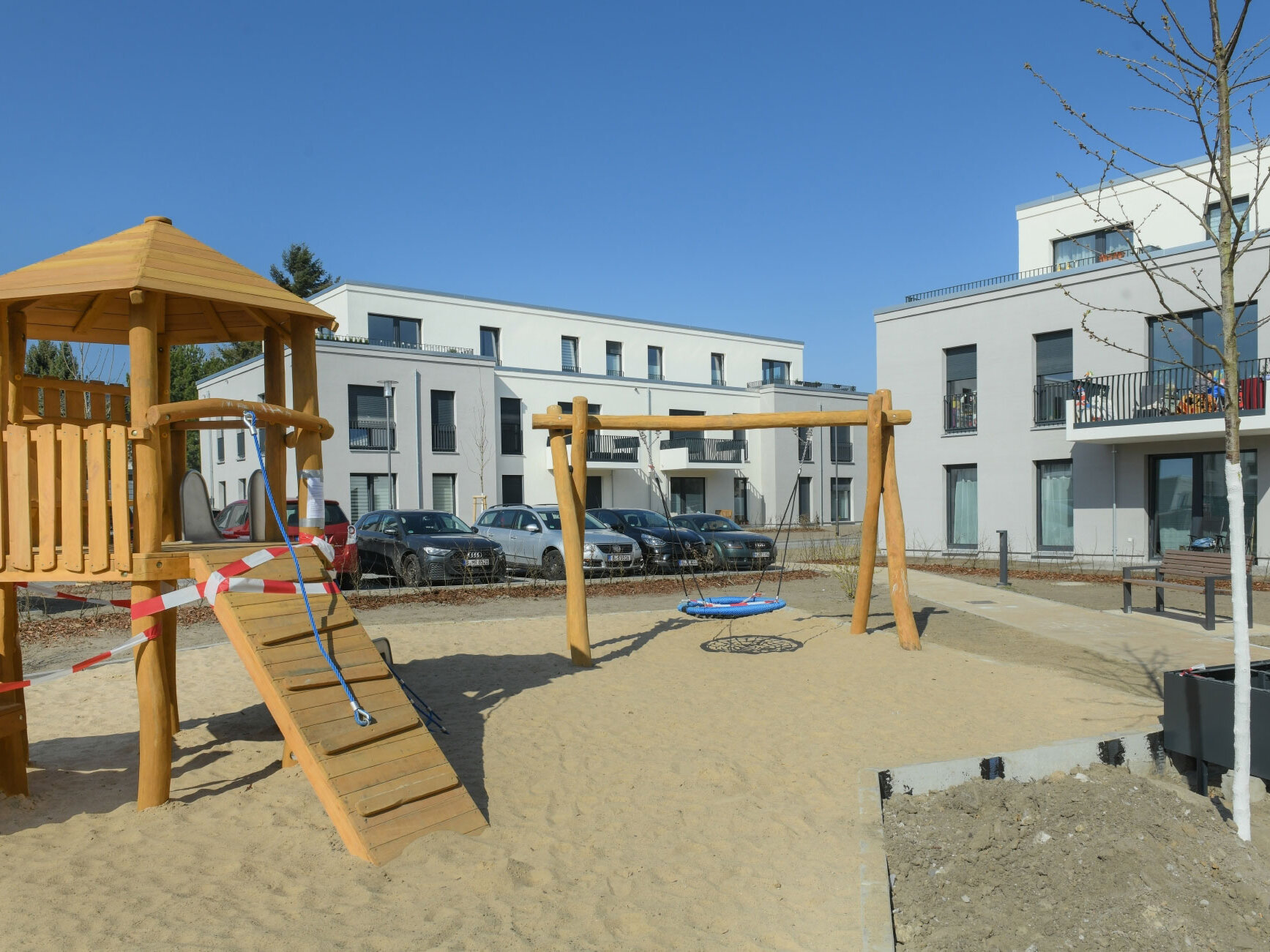 Außenansicht degewo-Neubau Bohnsdorfer Weg 127 bis 131 Knospengrund 27 bis 33 mit Spielplatz und neu gepflanztem Baum im Vordergrund.