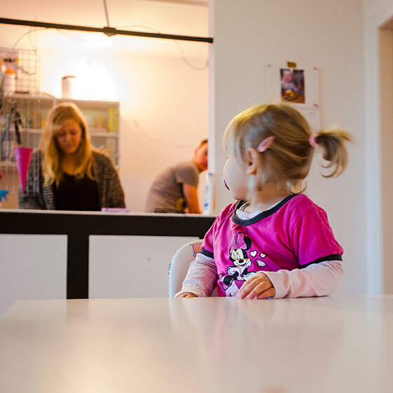 Kleinkind sitzt am Tisch und schaut nach hinten zur Mutter.