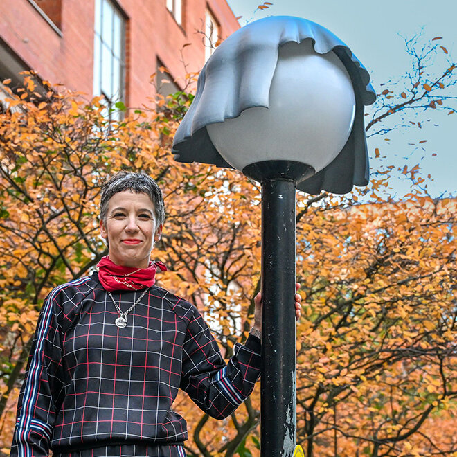 Frau steht an einer Laterne gelehnt. Die Laterne trägt eine Mütze.