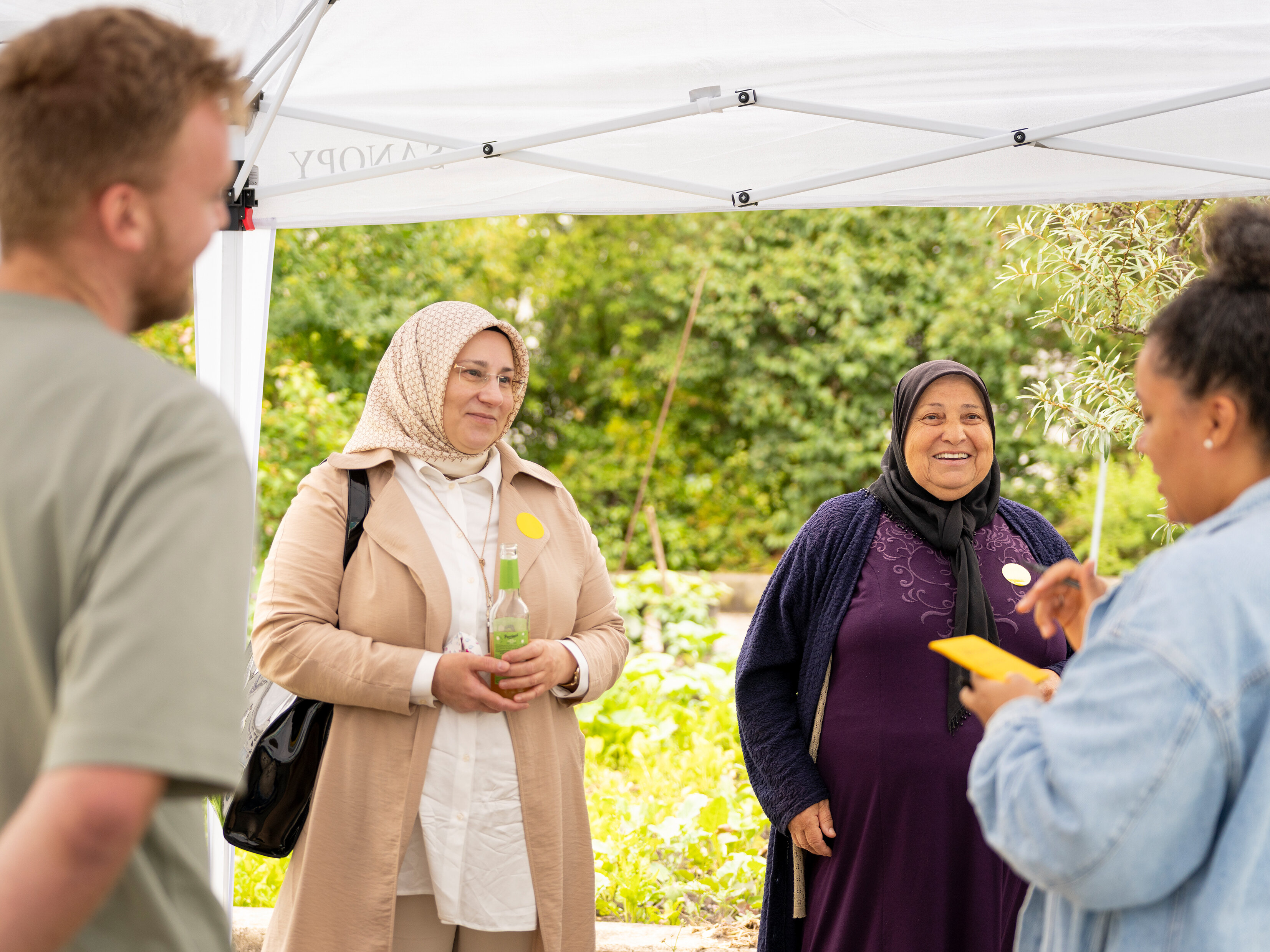 Kleine Gesprächsgruppe unter einem Pavillon im begrünten Innenhof. Zwei Teilnehmerinnen und eine Mitarbeiterin tauschen sich über Ideen zur Umgestaltung aus.