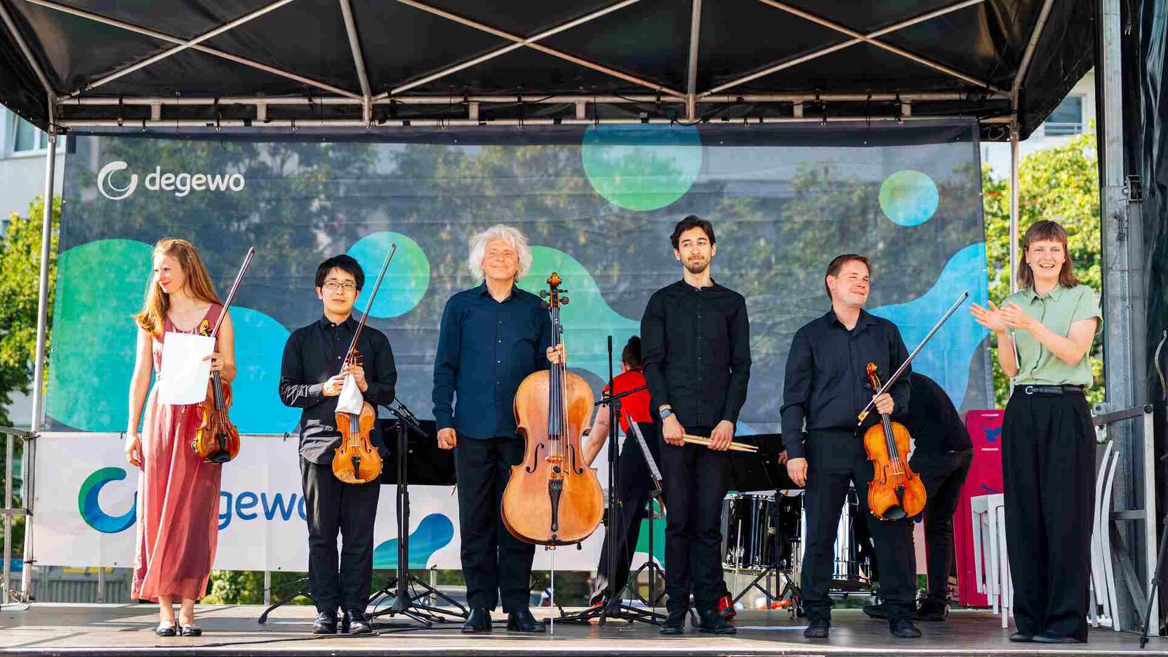 Sechs Musiker stehen auf einer Bühne mit Instrumenten und lachen ins Publikum.