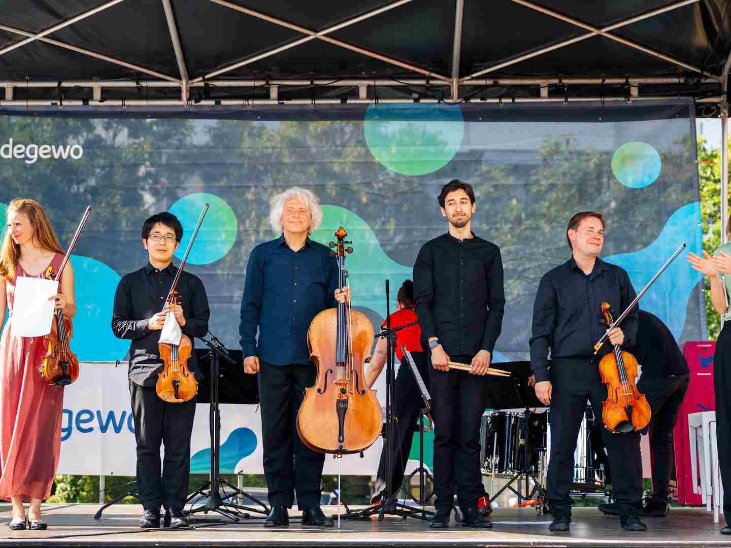 Sechs Musiker stehen auf einer Bühne mit Instrumenten und lachen ins Publikum.