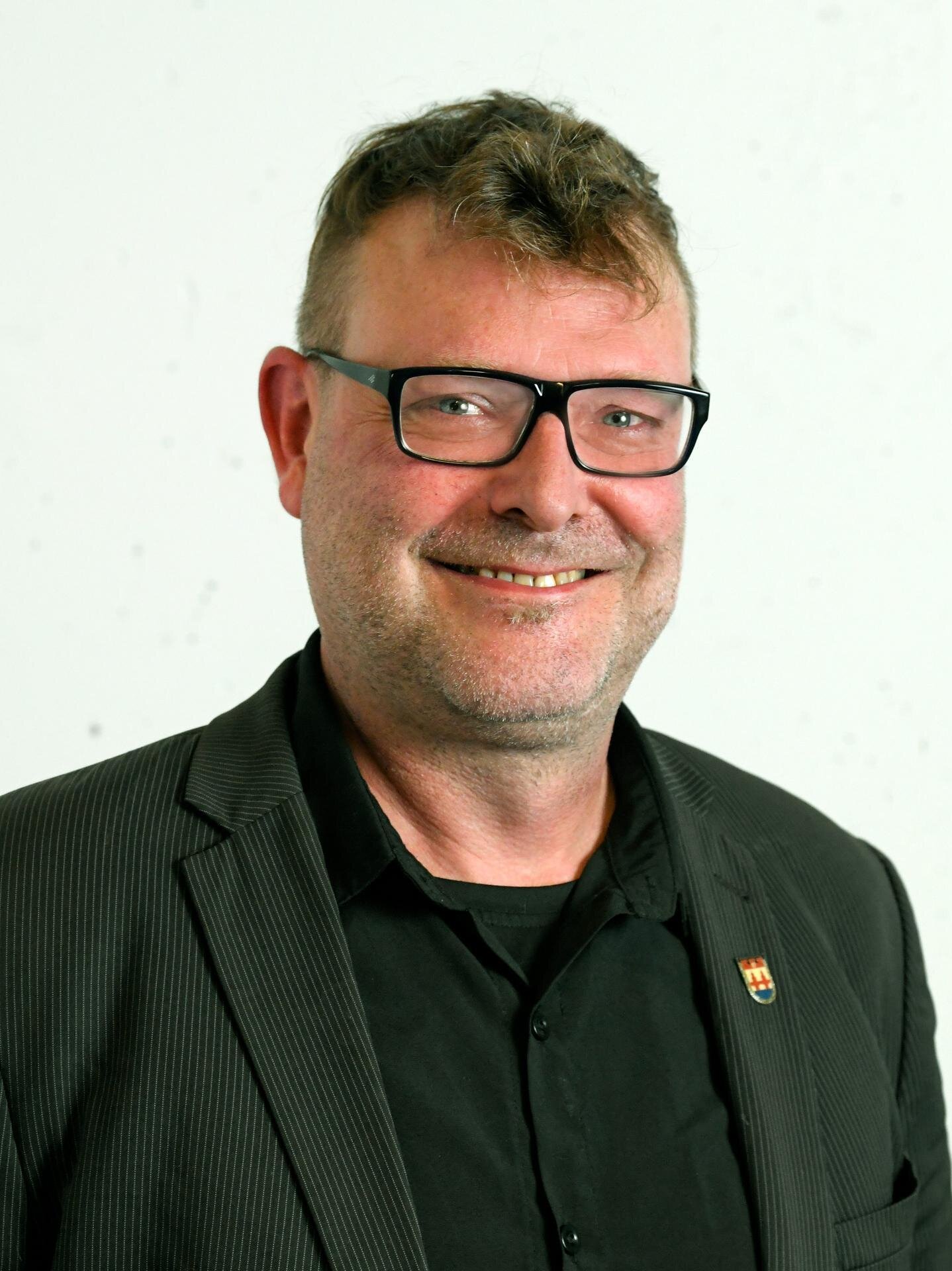 Porträt des Beiratsmitglieds Thorsten Buhl mit Brille und dunklem Sakko vor hellem Hintergrund.