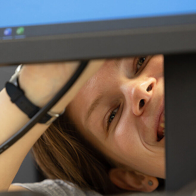 Frau guckt unter Bildschirm hervor und lacht