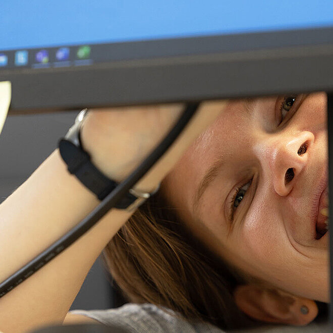 Frau guckt unter Bildschirm hervor und lacht