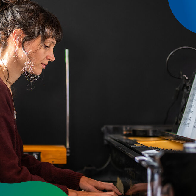 Eine Frau spielt an einem alten Klavier. Sonnenstrahlen scheinen von hinten auf sie. 