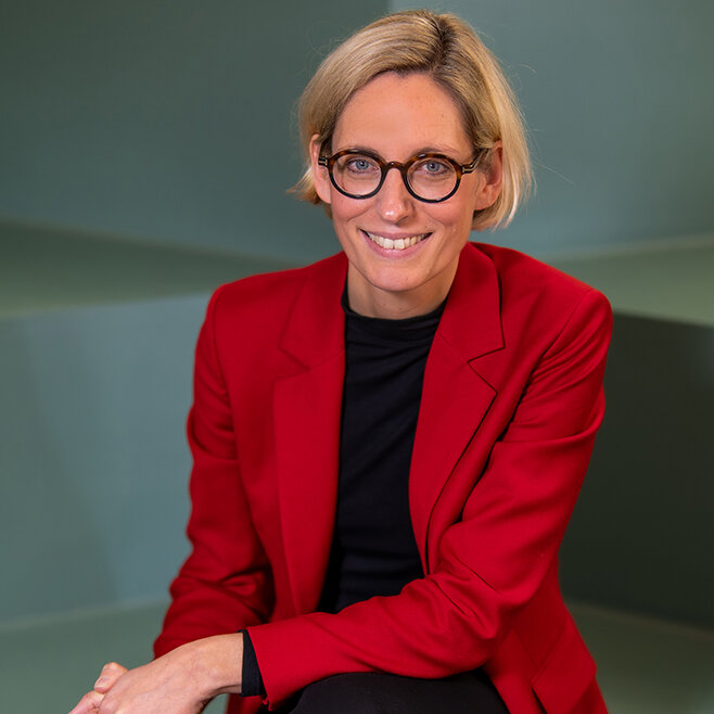 Eine Frau in einem roten Blazer sitzt lächelnd auf einer Treppe während ein degewo Logo mit der Aufschrift Wir sind degewo eingeblendet ist.