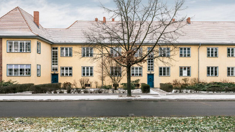Eine sanierte Wohnanlage mit heller Fassade, modernen Fenstern und begrüntem Vorgarten erstreckt sich entlang einer ruhigen Straße.