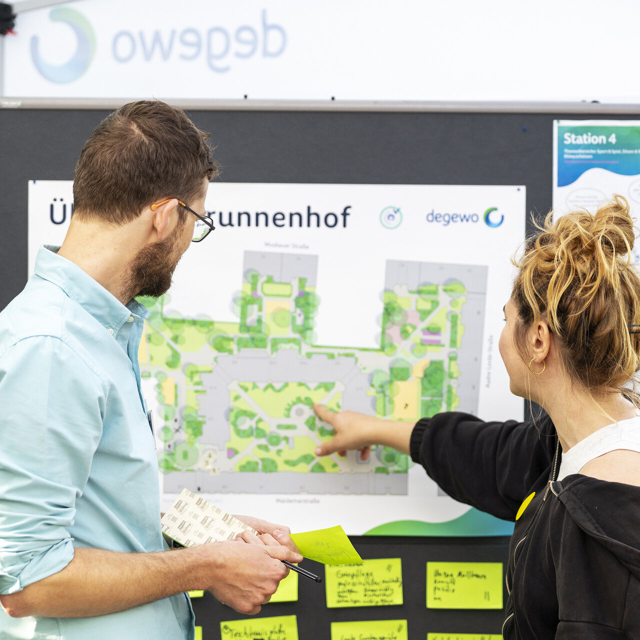 Ein Mitarbeiter informiert eine Anwohnerin über geplante Maßnahmen an einer Informationstafel.