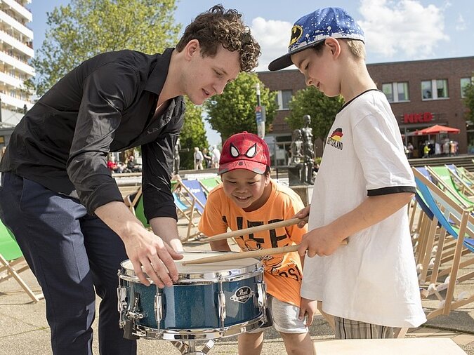 Ein junger Mann trommelt mit zwei Kindern