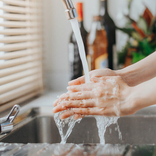 Person wäscht Hände unter laufendem Wasserhahn.