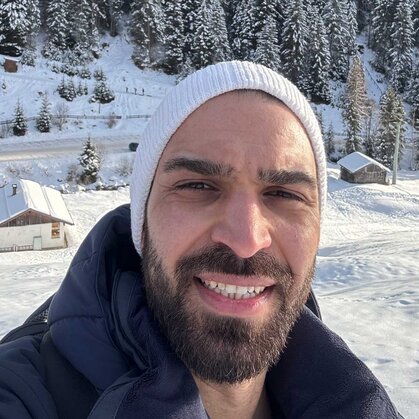 Ismail Kaya steht vor winterlicher Kulisse und lacht in die Kamera.