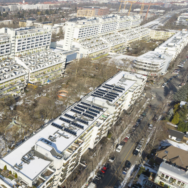 Luftaufnahme der Schlangenbader Straße in Berlin mit den markanten terrassenförmigen Wohngebäuden und verschneiten Dächern, umgeben von Stadtvierteln und Straßen.