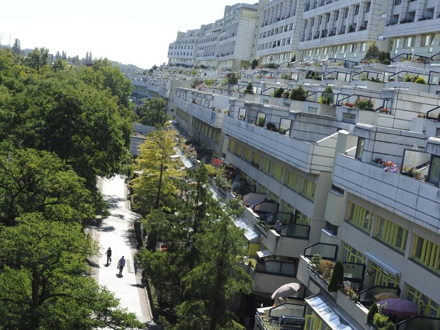 Blick von oben auf einen Fußgängerweg vor dem weißen Gebäude mit vielen Bäumen