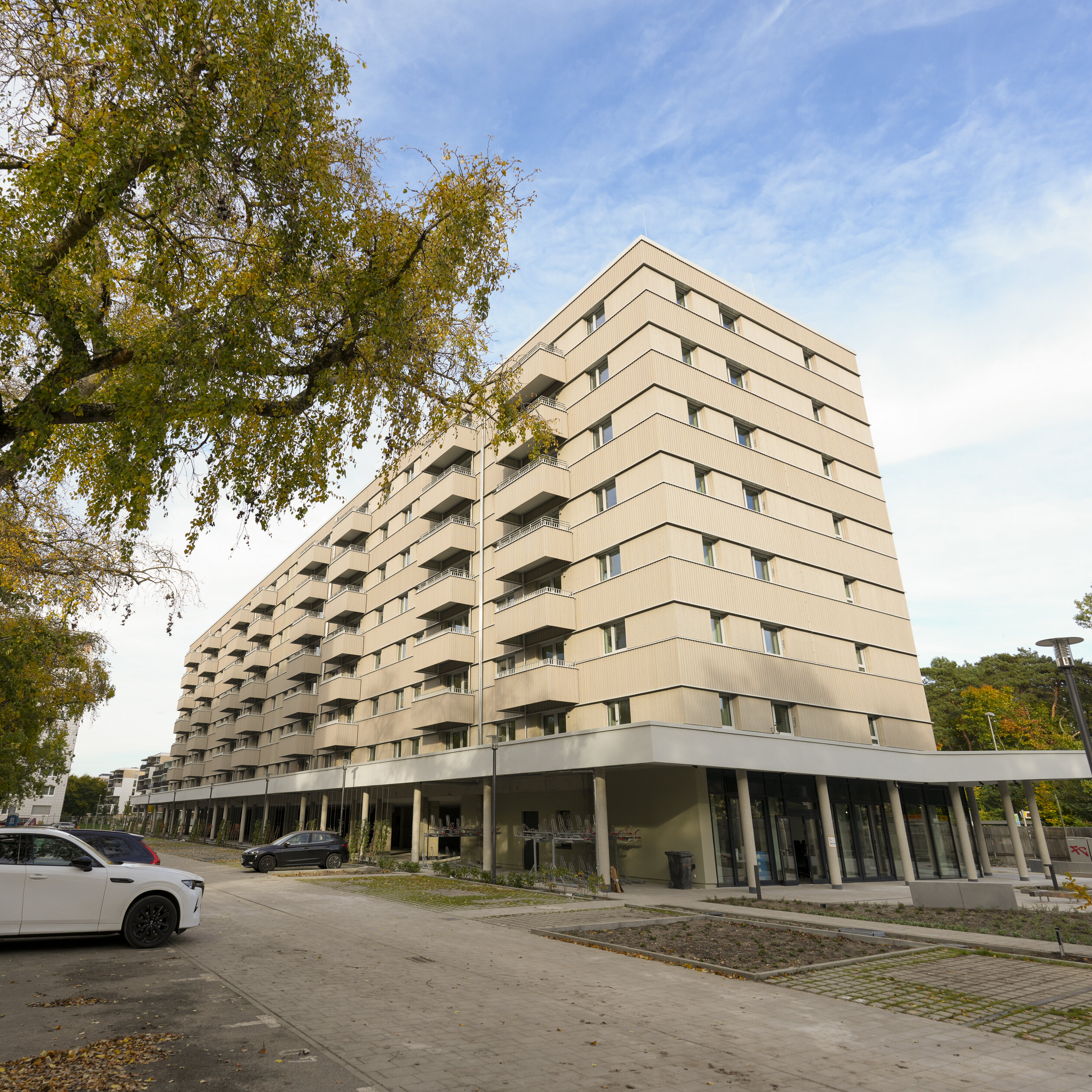 Langes Wohnhaus mit Balkonen an einer ruhigen Straße mit parkenden Autos.