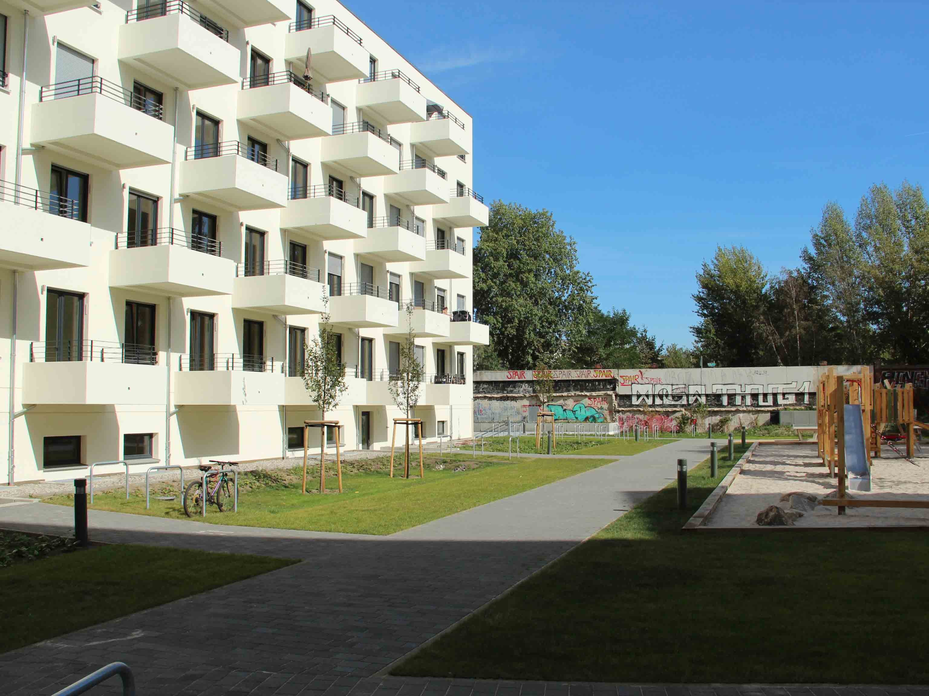 Außenansicht degewo-Neubau Graunstraße Gleimstraße: Hofseite mit Spielplatz sowie Wegen und Rasenflächen im Vordergrund.