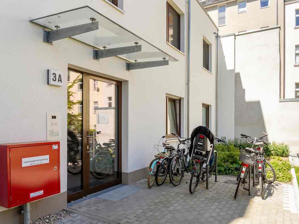 Außenansicht degewo-Neubau Glasoer Straße 3 A: Eingangsbereich mit Kasten für Löschwassereinspeisung und Fahrradständern.