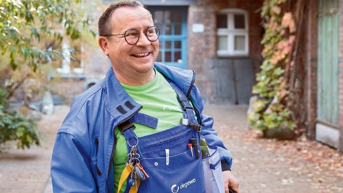 Ein Mann mit blauer Latzhose und Brille lacht.