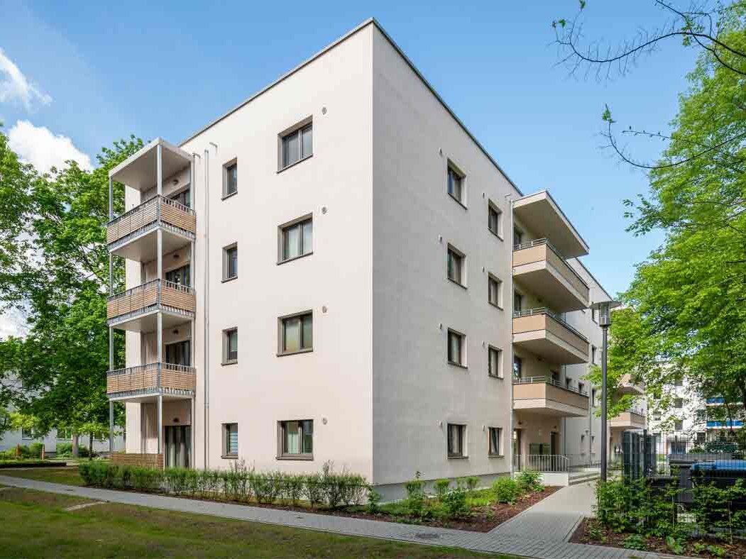 Außenansicht degewo-Neubau Färberstraße 19A mit Grünflächen, Wegen und beblätterten Bäumen im Vordergrund.