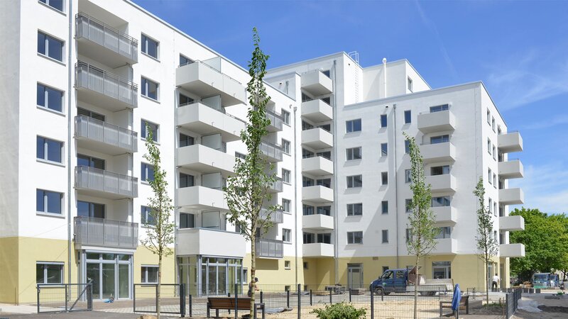 Außenansicht degewo-Neubau Agnes-Straub-Weg 22 mit Sandfläche und neu gepflanzten Bäumen im Vordergrund.