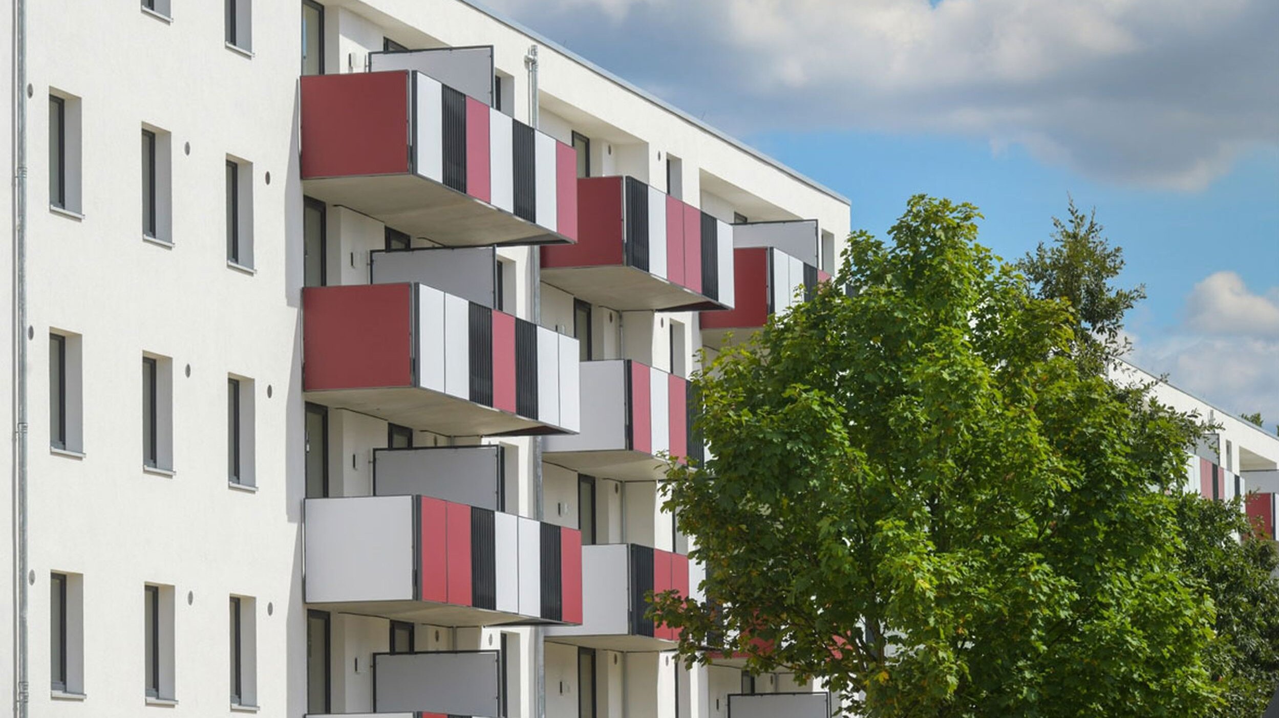 Außenansicht degewo-Neubau Schönefelder Chaussee 26 bis 38 Wegedornstraße 119 bis 123: Fassade mit Balkonen und Bäumen rechts.