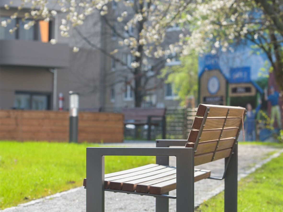 Außenansicht degewo-Neubau Venusstraße 28 mit Grünflächen, Weg, Sitzbank und blühendem Baum im Vordergrund.