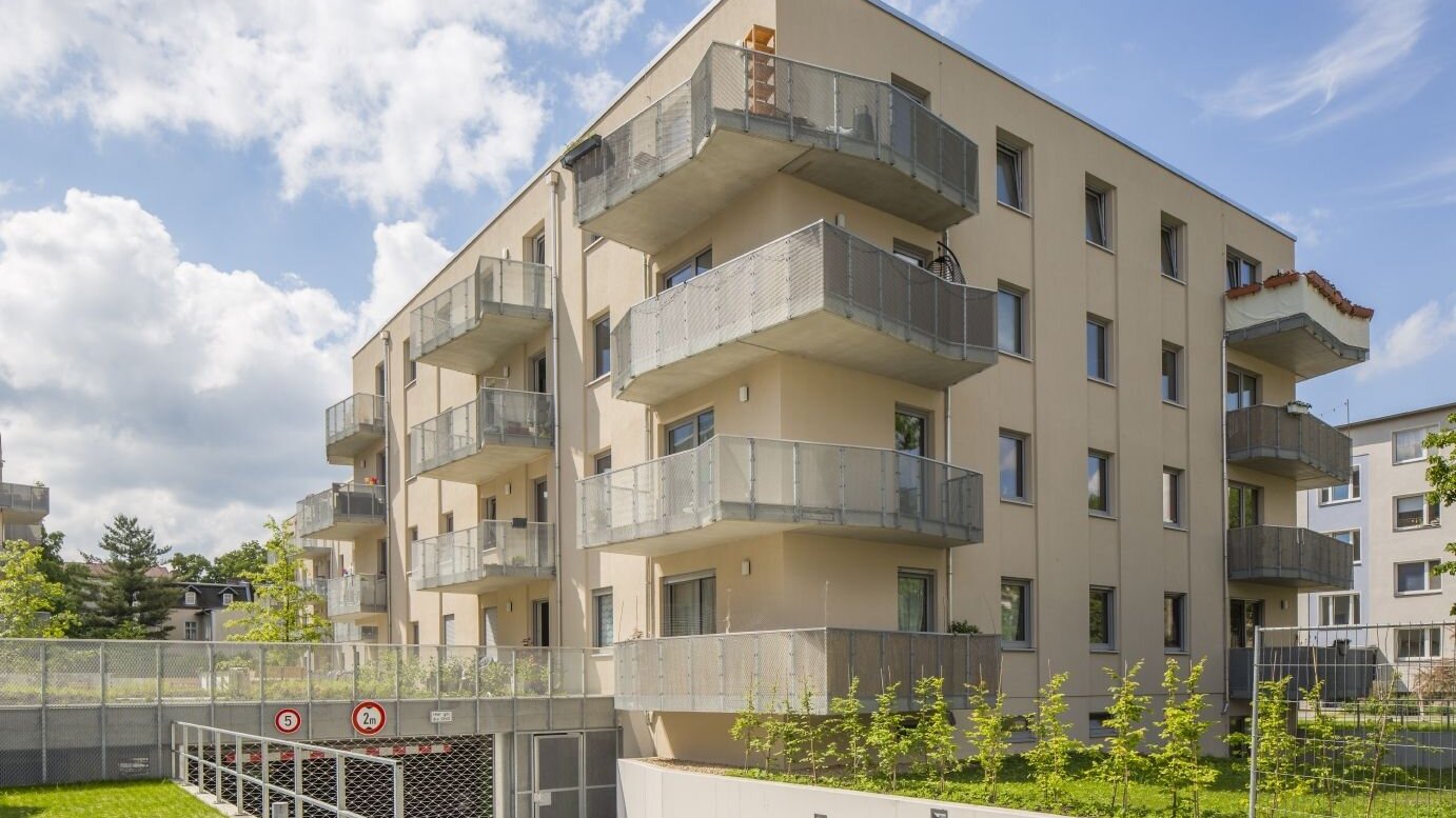 Moderner Wohnungsneubau mit hellen Fassaden, großzügigen Balkonen und integrierter Tiefgarageneinfahrt in einem ruhigen Berliner Wohngebiet mit Grünflächen.