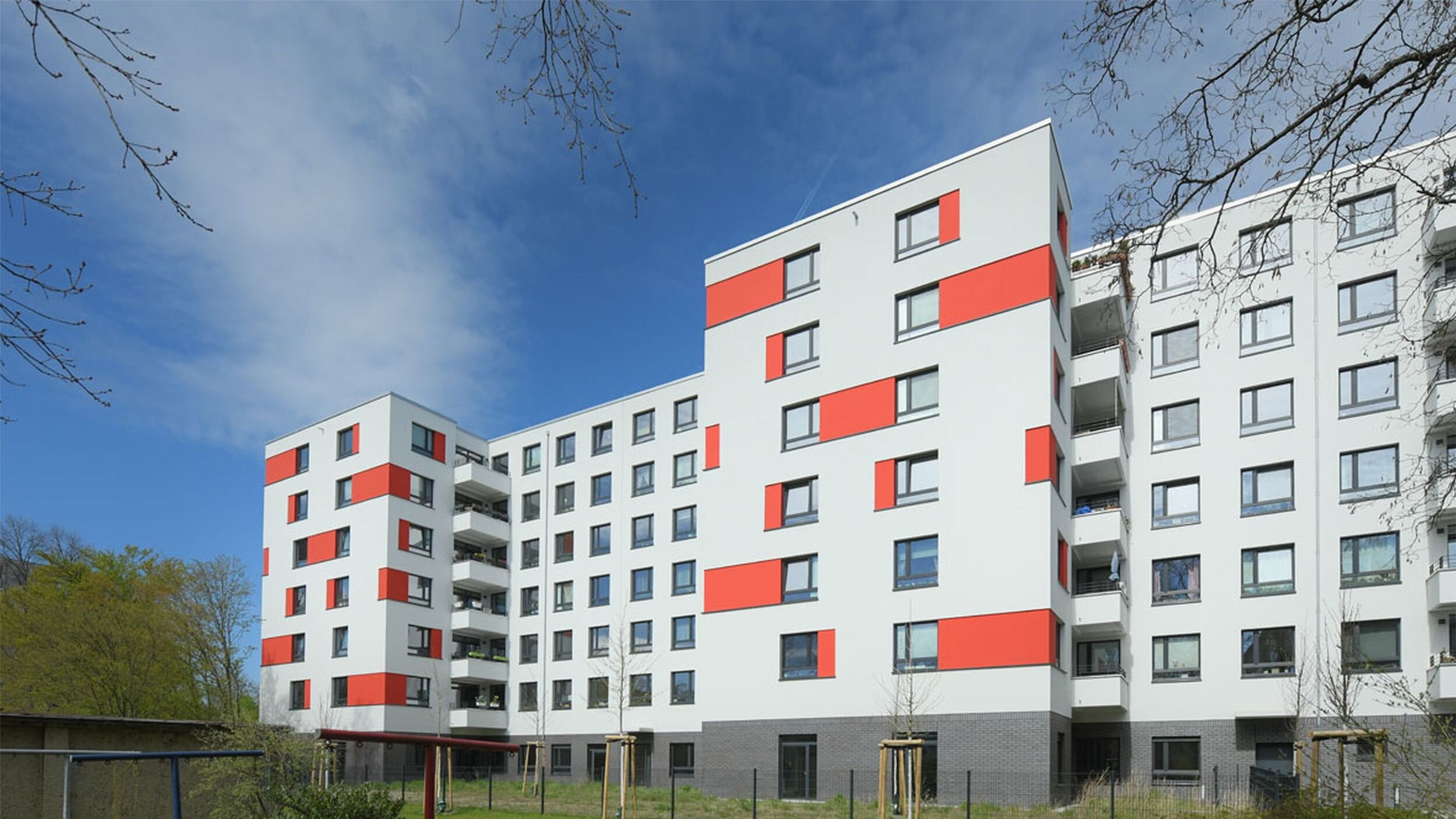 Außenansicht degewo-Neubau An der Wuhlheide 112 bis 116: Hofseite mit Grünflächen, Weg, Maschendrahtzaun, neu gepflanzten Bäumen und Wäscheleinen im Vordergrund.