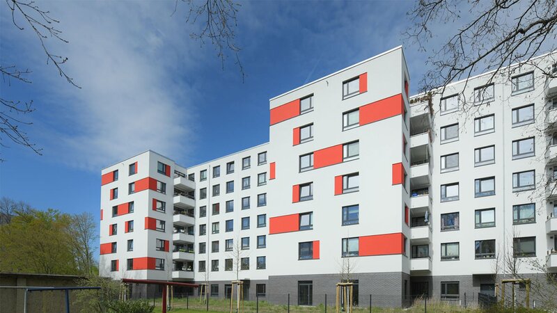 Außenansicht degewo-Neubau An der Wuhlheide 112 bis 116: Hofseite mit Grünflächen, Weg, Maschendrahtzaun, neu gepflanzten Bäumen und Wäscheleinen im Vordergrund.