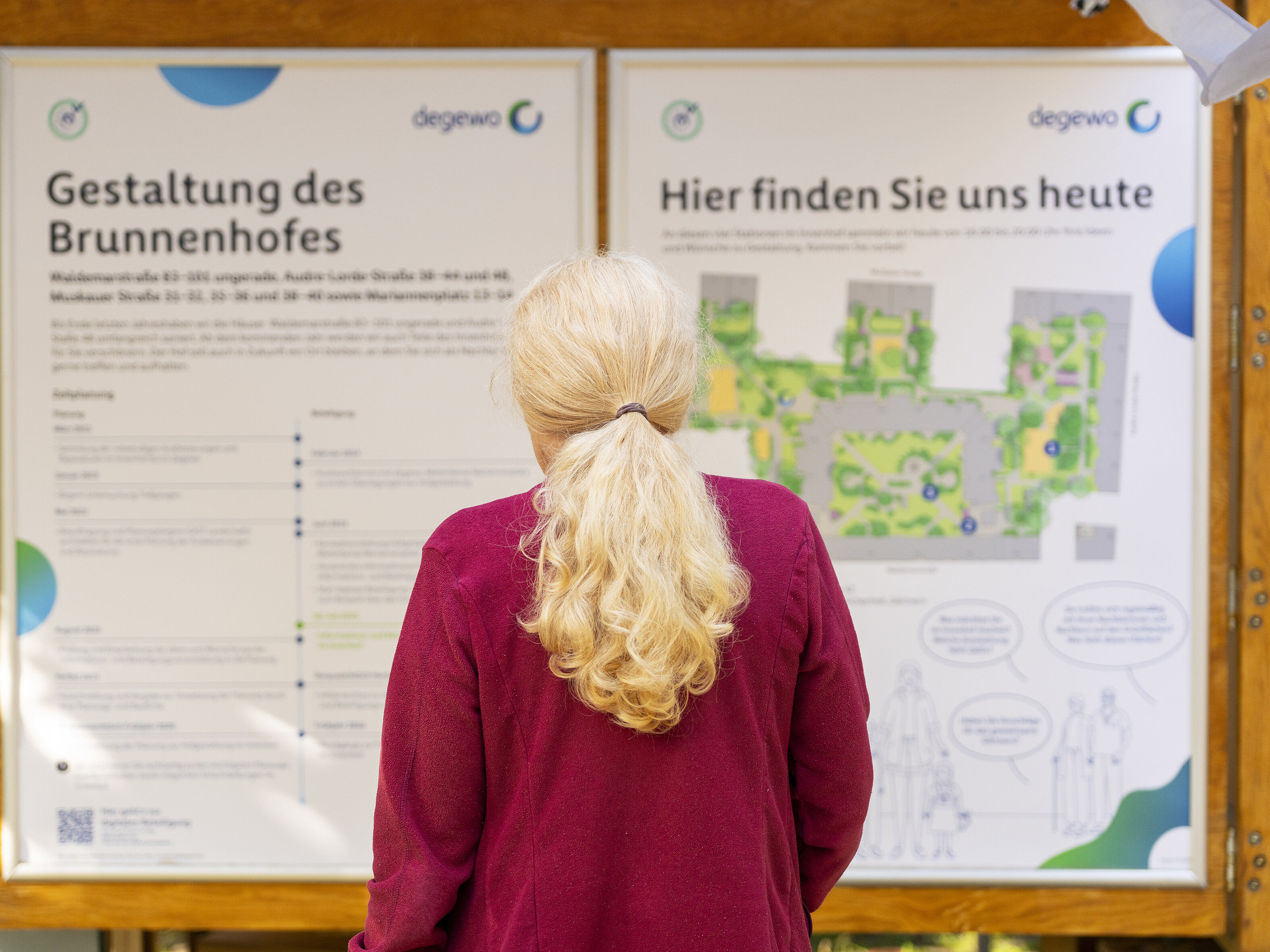 Besucherin betrachtet eine Übersichtstafel zur Gestaltung des Brunnenhofes mit Lageplan und Erläuterungen.