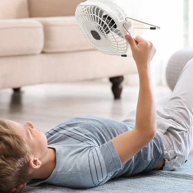 Junge liegt auf dem Boden und richtet einen Ventilator auf sich