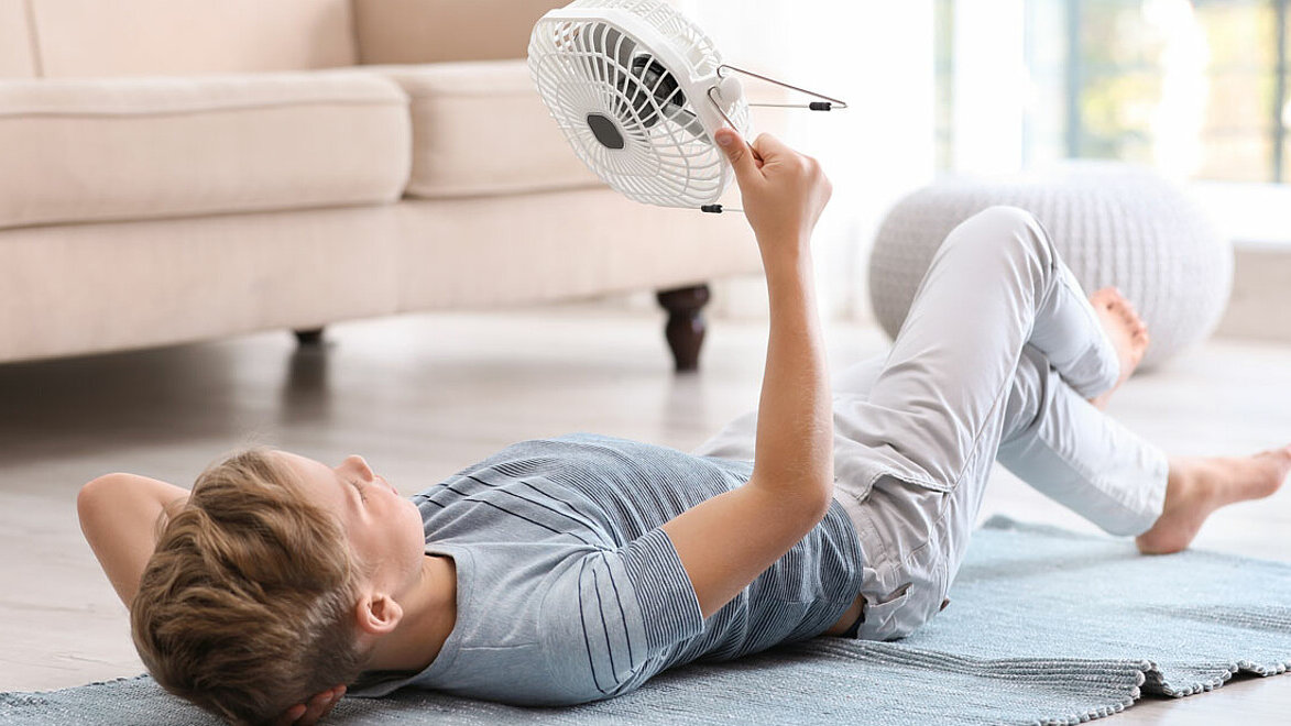 Junge liegt auf dem Boden und richtet einen Ventilator auf sich