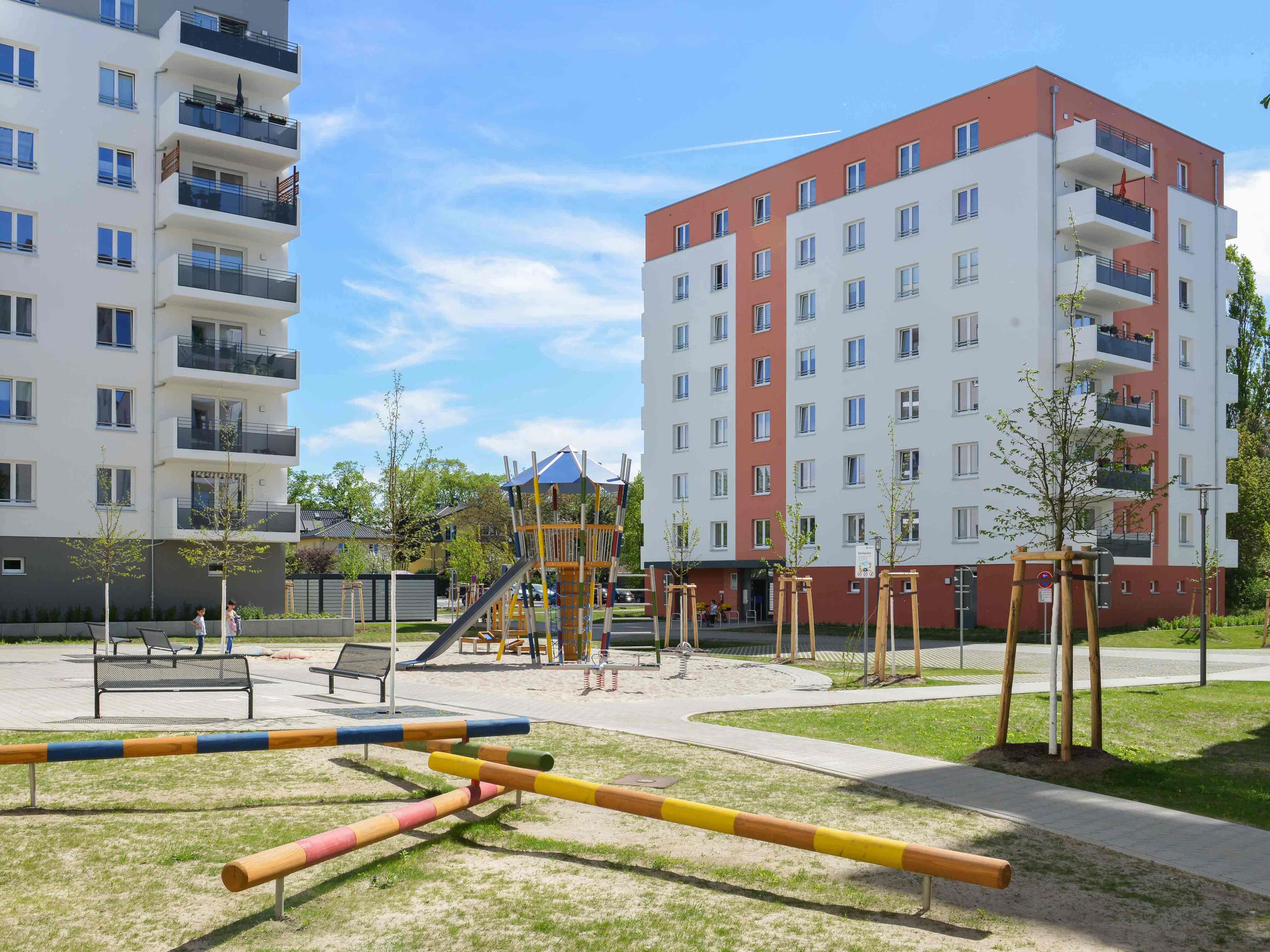 Außenansicht degewo-Neubau Eugen-Roth-Weg 4 bis 10 mit neu gepflanzten Bäumen, Bänken und Spielplatz im Vordergrund.