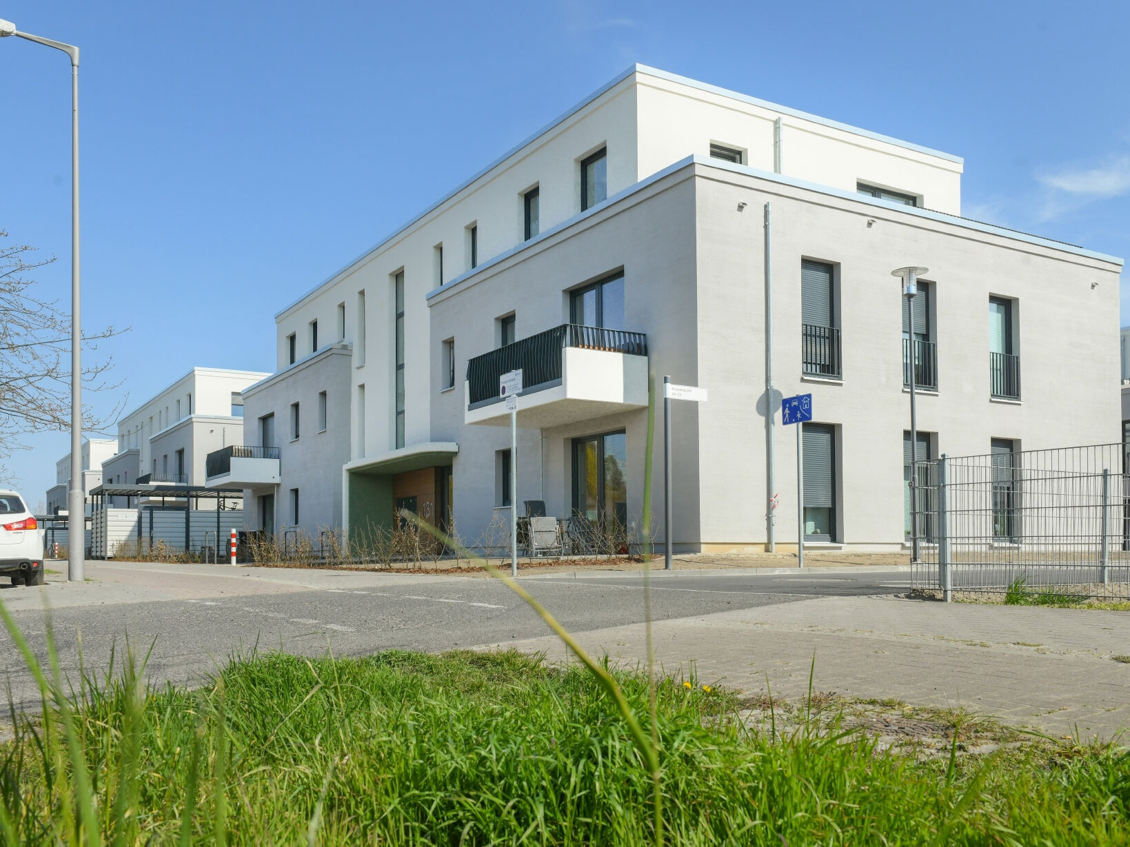 Außenansicht degewo-Neubau Bohnsdorfer Weg 127 bis 131 Knospengrund 27 bis 33 mit Grünfläche, Parkflächen und Straße im Vordergrund.