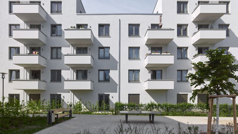 Außenansicht degewo-Neubau Dessauerstraße 39 bis 45 a-b Retzowstraße 54 bis 60: Hofseite mit Sitzbank, Tischtennisplatte und rechts neu gepflanztem Baum sowie Sträuchern im Vordergrund.