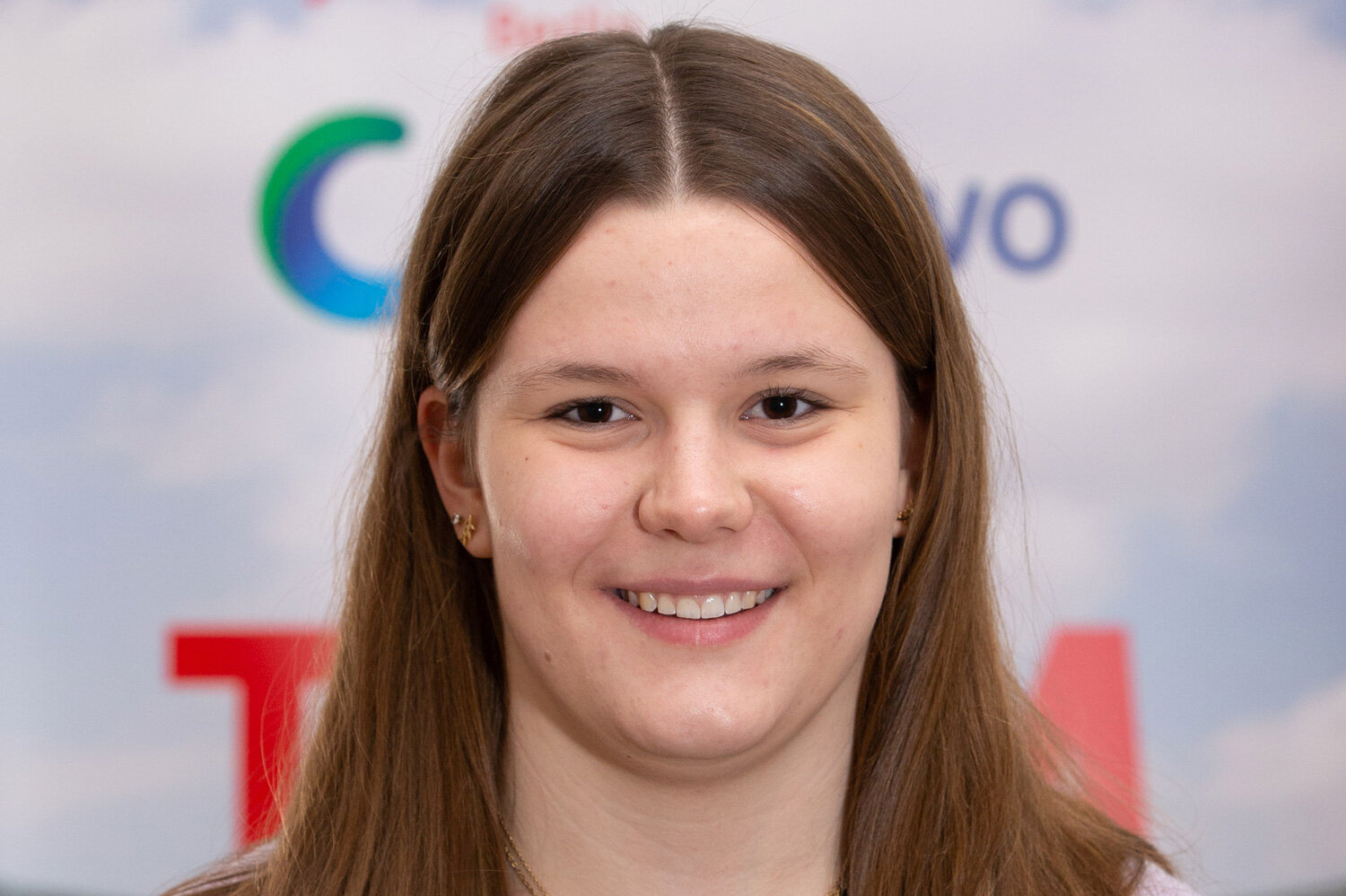 Junge Frau mit braunen Haaren lächelt in die Kamera. Der Hintergrund zeigt eine Sponsorenwand mit degewo-Logo.