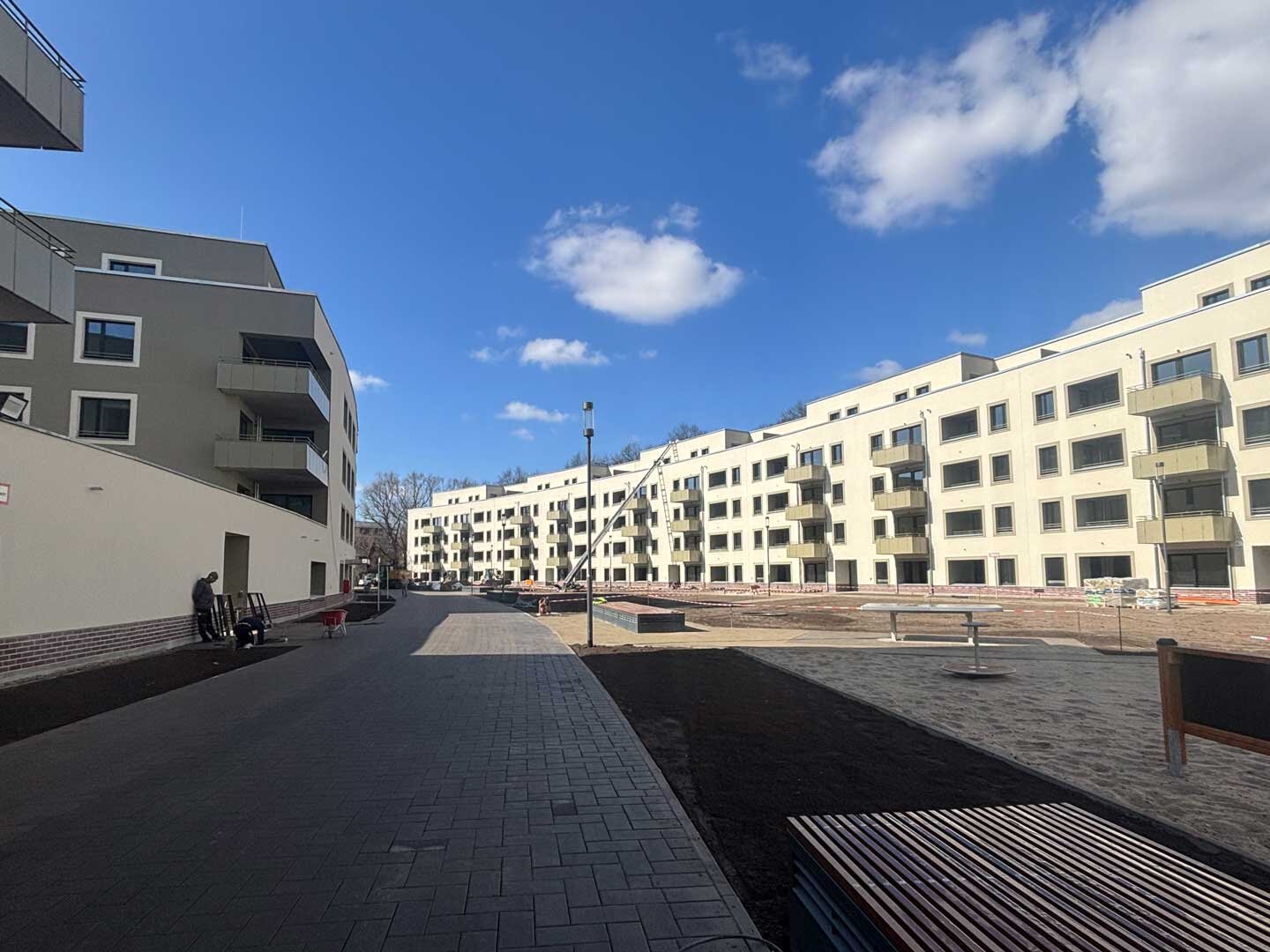Außenansicht der Wohnanlage im Halbschatten. Es sind ein Sandkasten und Kräne zu sehen, neben der Gebäude.