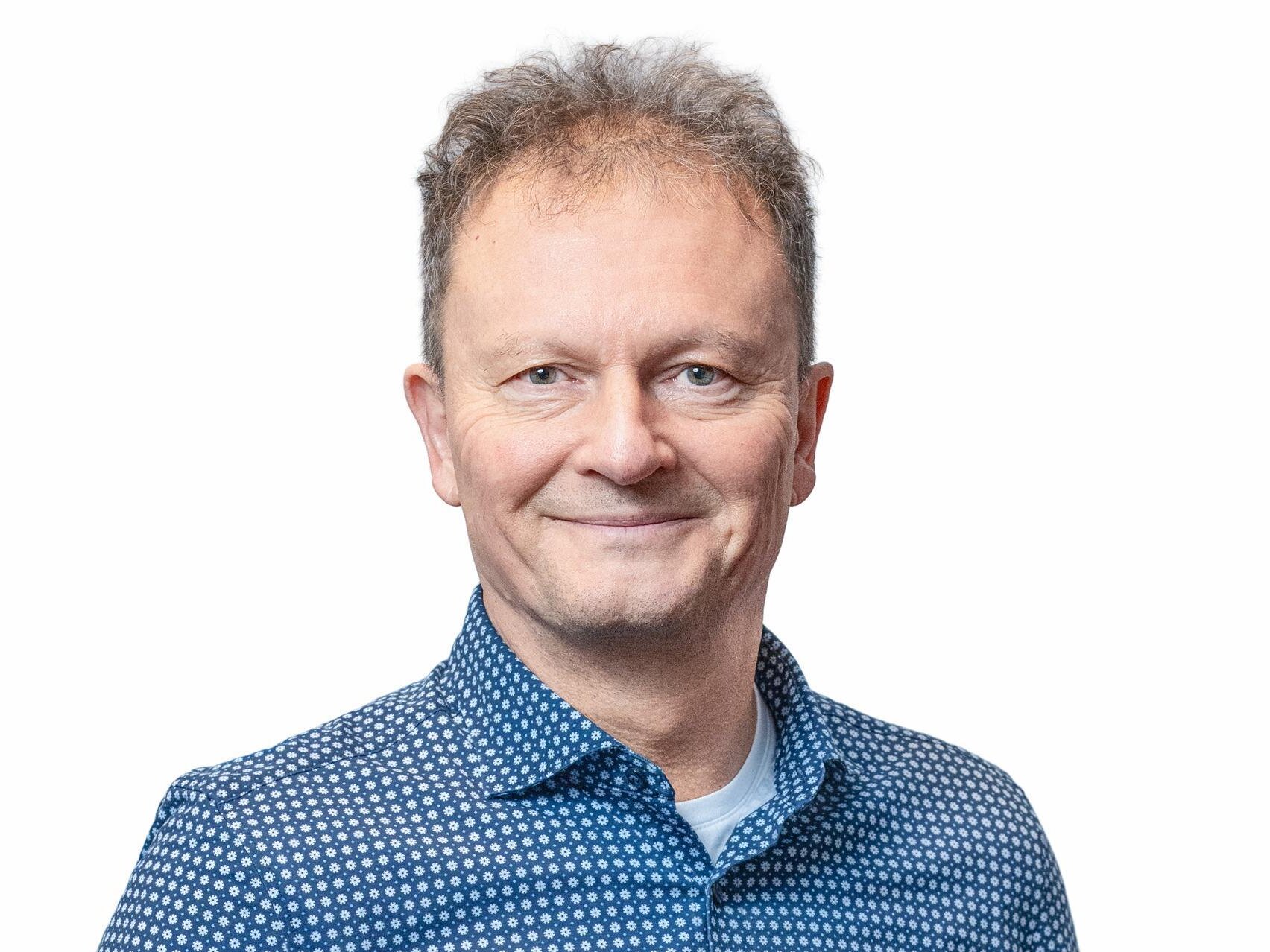 Ein älterer Herr mit kurzen Haaren und blauem Hemd lächelt freundlich in die Kamera.