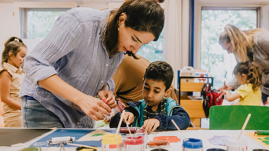 Ein kleines Kind wird beim Basteln durch eine Erwachsene angeleitet