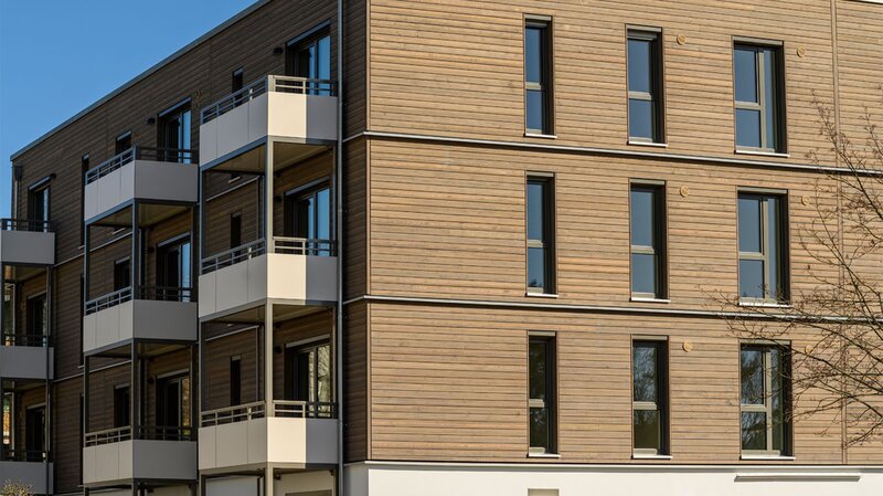 Außenansicht degewo-Neubau Am Omnibushof 2a mit unbeblätterten Baumzweigen rechts im Vordergrund.