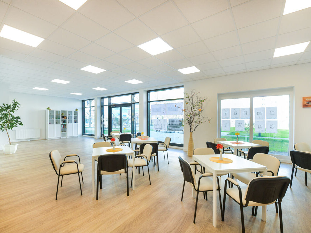 Innenansicht degewo-Neubau Venusstraße 28: beleuchteter Saal mit quadratischen Tischen und je vier Stühlen im Vordergrund.