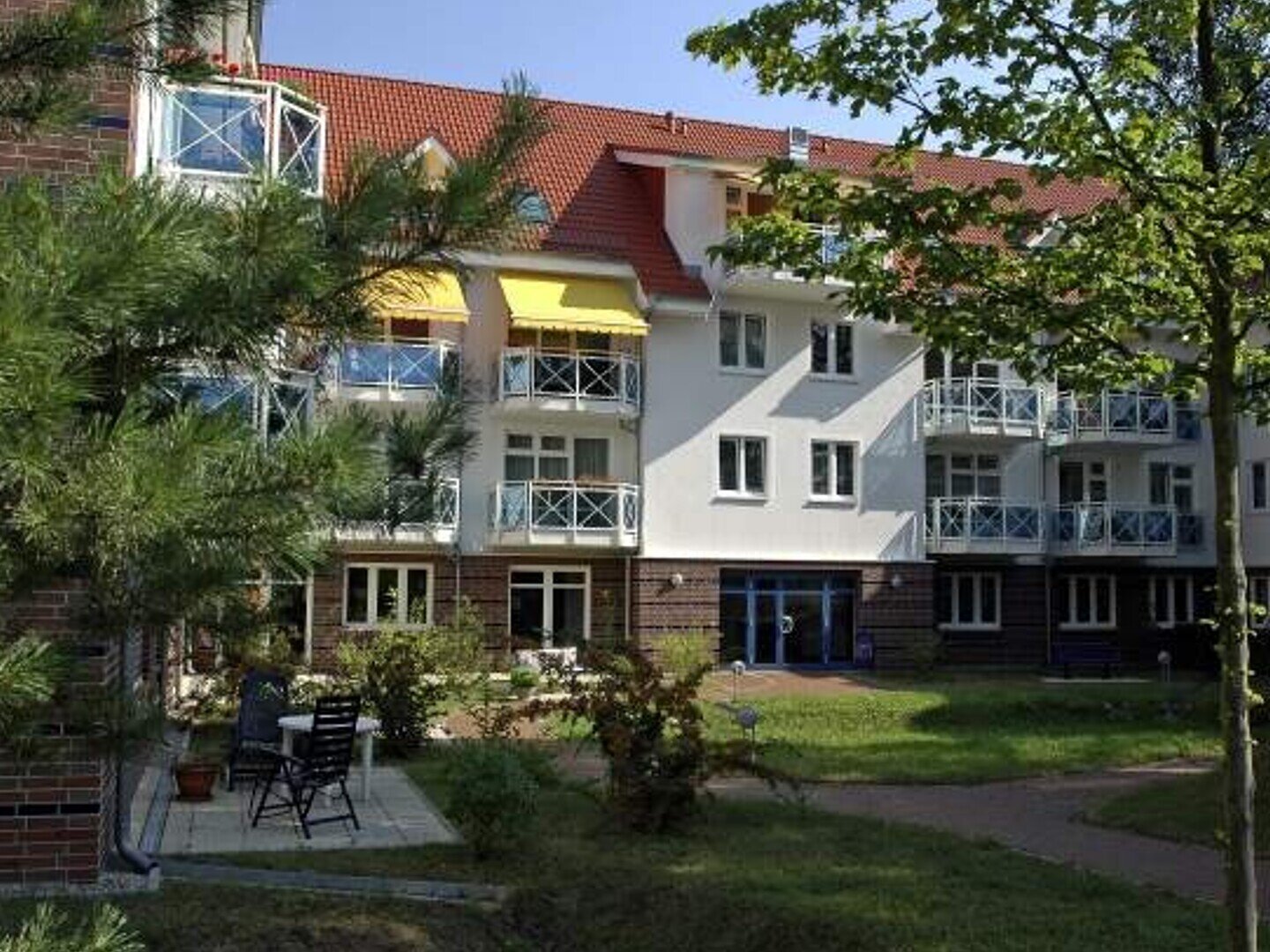 Blick durch die Bäume auf die Seniorenresidenz, ein weißes Haus mit Balkonen und gelben Markisen