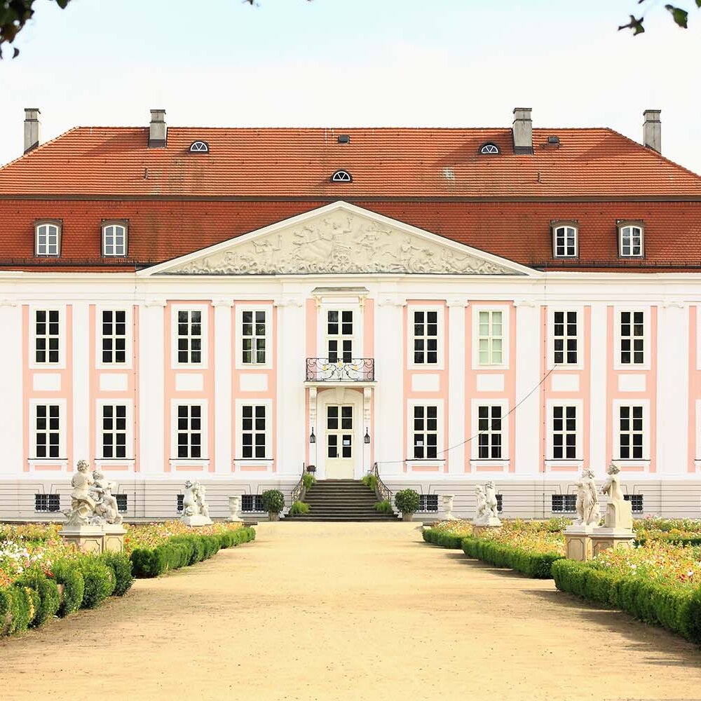 Historisches Schloss mit heller Fassade, rotem Dach und symmetrisch angelegtem Gartenweg.