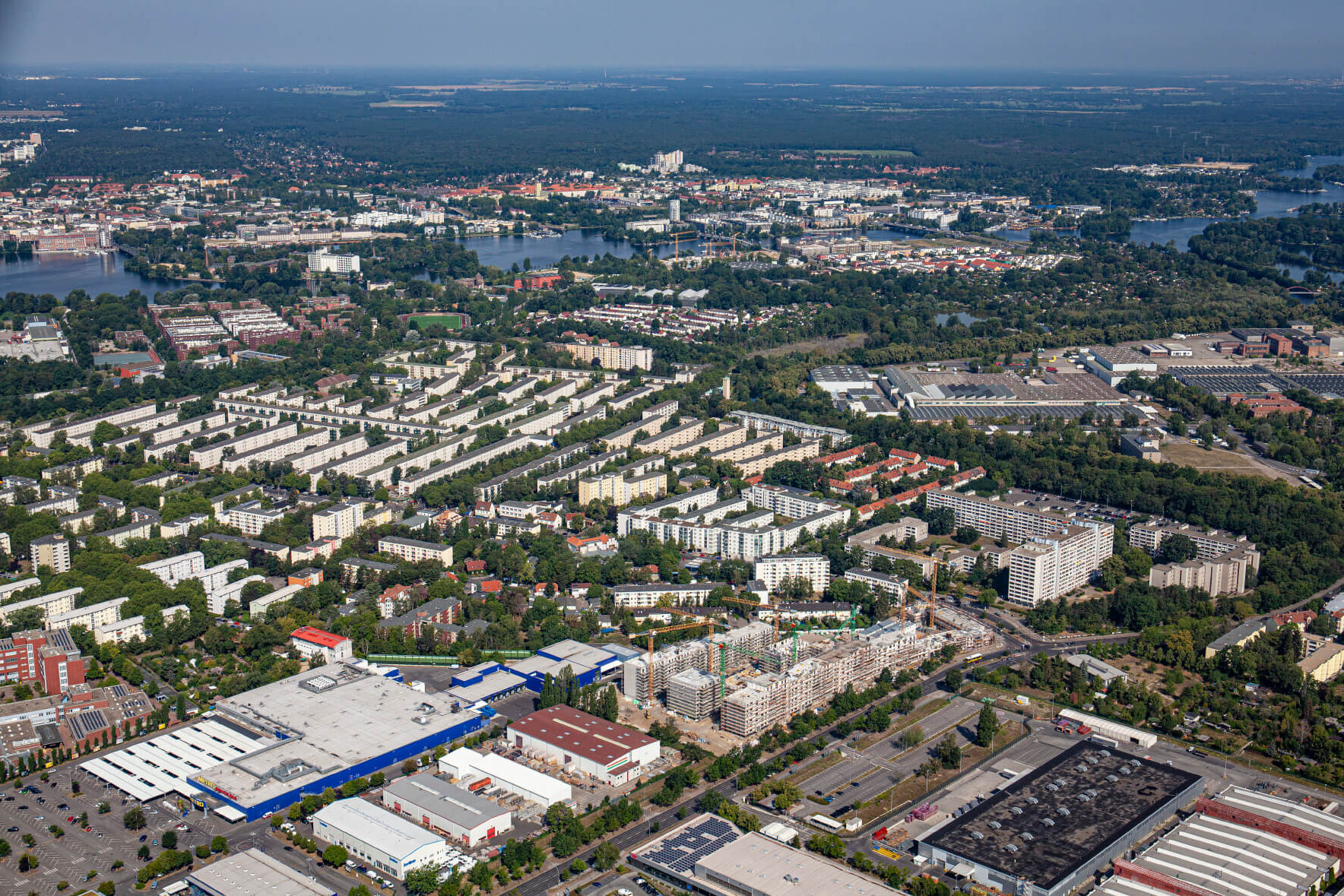 Ein Luftbild zeigt ein Wohngebiet in Berlin Spandau mit mehreren Wohnblöcken, Baustellen, Gewerbeflächen und viel Grün aus der Vogelperspektive.
