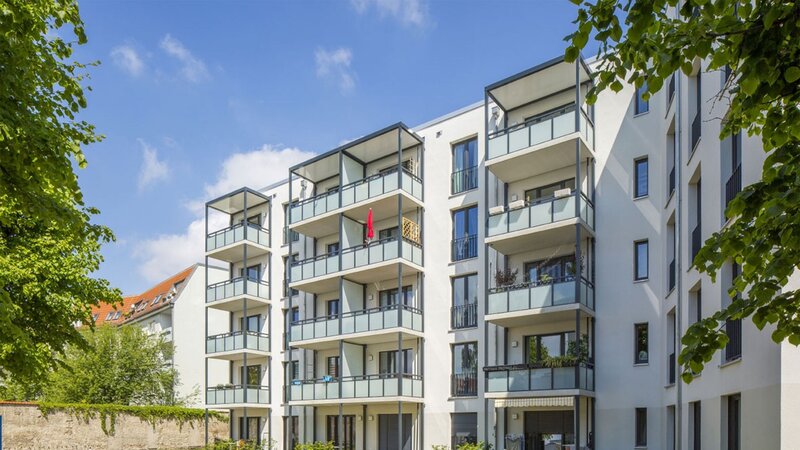 Außenansicht degewo-Neubau Luisenstraße 24 bis 24 A: Hofseite mit Grünfläche und beblätterten Zweigen links und rechts im Vordergrund.