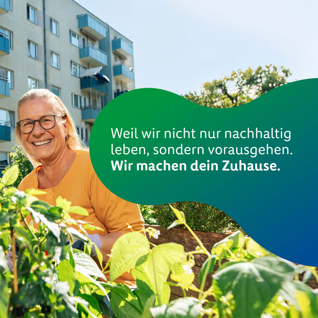 Zwei Personen sitzen in einem begrünten Innenhof vor einem mehrgeschossigen Wohngebäude mit Balkonen und bepflanzen gemeinsam ein Hochbeet. Beide tragen Handschuhe und lächeln in die Kamera. Im Vordergrund sind grüne Pflanzen und Blätter zu sehen. Rechts im Bild befindet sich eine große grün-blaue Grafikfläche mit dem Schriftzug: „Weil wir nicht nur nachhaltig leben, sondern vorausgehen. Wir machen dein Zuhause.“