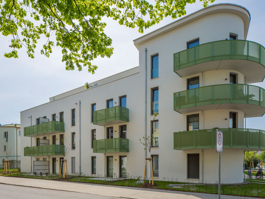 Straßenansicht degewo-Neubau Wassersportallee 13 mit blättrigen Baumzweigen oben im Vordergrund.