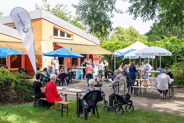 1. Sanierungscafé in der Horstwalder Straße: Die Anwohner sitzen in einem Garten auf Bierbänken an Tischen und lassen sich informieren.